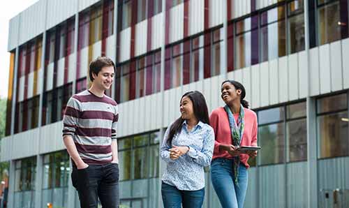 Three students laughing outside the learning commons at the University of Manchester
