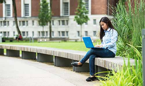 A student sitting on the University of Manchester campus with a laptop