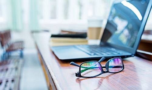 A laptop on a desk with some glasses next to the that in the foreground